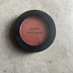 Gen Nude Powder Blush från bareMinerals - Säljer en Gen Nude Powder Blush i nyansen 'But First, Coffee' från bareMinerals. Denna rouge har en varm, brunaktig ton och kommer i en rund förpackning med genomskinligt lock. Perfekt för att ge kinderna en naturlig glöd.