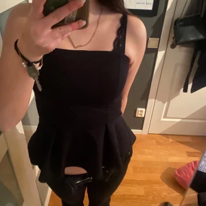 Svart ärmlös topp med spetsdetaljer - Snygg svart ärmlös topp . Toppen har en peplumdesign som ger en fin siluett. Perfekt för en kväll ute eller en speciell tillställning.