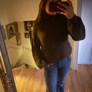 Olivgrön stickad polotröja - Säljer en mysig olivgrön stickad polotröja med kabelstickat mönster. Tröjan har långa ärmar och en hög krage från NA-KD i storlek xs men passar mig som bär M