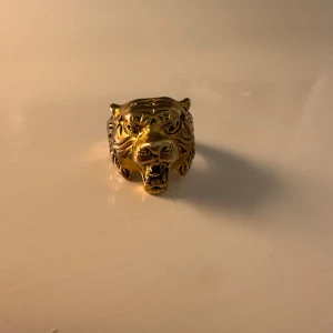 Lejon ring - Guldig lejon ring med lite missfärgningar. Unik guldfärgad ring formad som ett tigerhuvud. Ringen har detaljerade drag och en djärv design som verkligen sticker ut. Perfekt för att ge en outfit en extra edge.