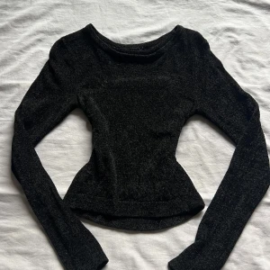 Svart långärmad topp från Bik Bok - Snygg svart långärmad topp från Bik Bok i ett fluffigt material. Perfekt för att lägga till lite glamour i din garderob. Toppen har en figurnära passform och är tillverkad i ett mjukt och bekvämt tyg.