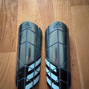 Fotboll benskydd Adidas X Pro  - Säljer ett par Adidas X Pro benskydd i svart och blåsilver. De har en modern design med skyddande paneler och kommer med svarta strumpor för extra komfort. Perfekt för fotbollsspelare som söker stil och säkerhet på planen. Perfekt storlek för någon som är runt 165-175cm lång