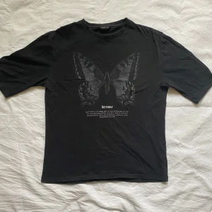 Svart t-shirt med fjärilstryck från Even&Odd - Säljer en svart t-shirt från Even&Odd med ett stort fjärilstryck på framsidan. T-shirten har lite längre ärmar och något oversized passform