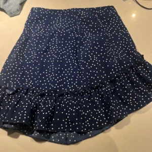 Blå prickig kjol från Shein - Säljer en söt blå kjol med vita prickar från Shein. Kjolen har en volangdetalj längst ner och en dragkedja i sidan💙