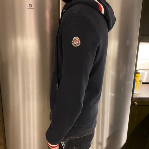 Moncler Zip Hoodie - Säljer en riktigt shysst Moncler hoddie då den har växt ur mig och ligger mest i garderoben. Tröjan är i väldigt bra skick då den inte har några hål eller fläckar. Storlek M men passar S också. Säljes billigt pågrund av inget Kvitto eller låda. Vid fler frågor tveka inte på att höra av dig. Mvh Ludde