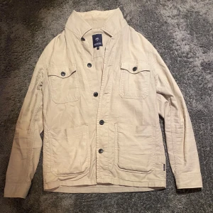 Beige overshirt från Lindbergh - Tjena, Säljer en stilren beige overshirt från Lindbergh, Perfekt för lager-på-lager-stil. Jag har bytt ut en av knapparna men det syns inte om man inte kollar noggrant. Overshirten har små tecken på användning och den är lite sliten vid fickorna men det syns också bara om man kollar noga på nära hål. Hör av dig vid funderingar 😁