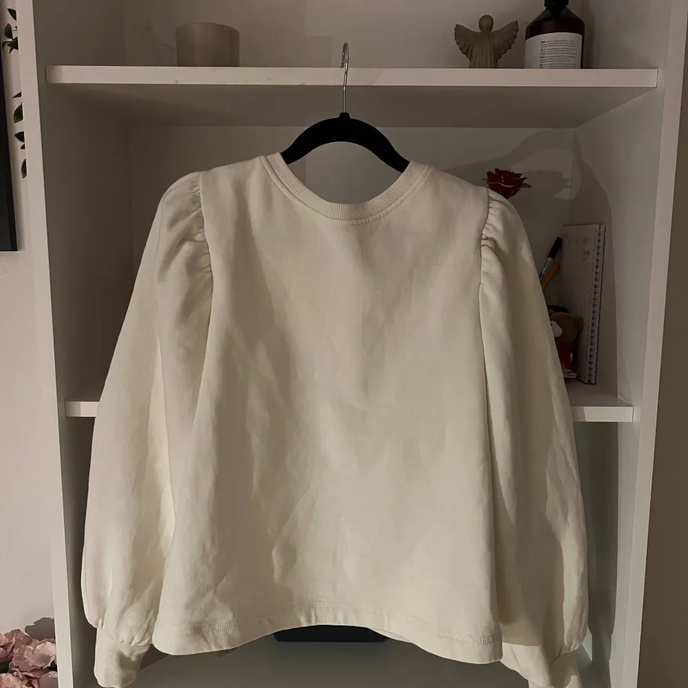 Säljer en stilren vit tröja med långa ärmar och en öppen rygg med knytband från H&M. Tröjan har en rund halsringning och puffiga ärmar som ger en trendig touch. Storlek M. Neuletakit & Villapaidat.