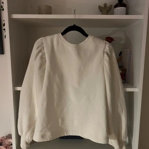 Vit tröja med knytband - Säljer en stilren vit tröja med långa ärmar och en  öppen rygg med knytband från H&M. Tröjan har en rund halsringning och puffiga ärmar som ger en trendig touch. Storlek M