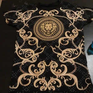 Svart t-shirt med lejonmotiv från Icono - Snygg svart t-shirt från Icono med ett stort lejonmotiv i mitten och dekorativa guldfärgade mönster. Perfekt för dig som vill sticka ut med en unik stil. T-shirten har korta ärmar och en slim fit passform.