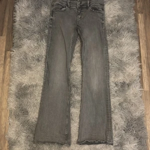 Grå bootcut jeans från Gina Tricot - Snygga grå jeans från Gina Tricot i bootcut-modell. Jeansen har en cool stjärndetalj på bakfickan och dubbla knappar framtill. Tillverkade i klassiskt jeanstyg med en lätt tvättad look. Perfekta för dig som gillar en avslappnad men trendig stil.