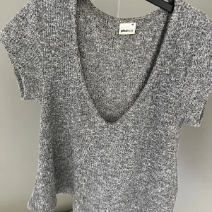 Grå ”ribbad” topp från Gina Tricot - Kortärmad ribbad topp i melerad grå färg från Gina Tricot. Modellen har djup v-ringning och en croppad passform som ger en chill vibe. Perfekt att matcha med jeans eller kjol för en enkel men snygg look.