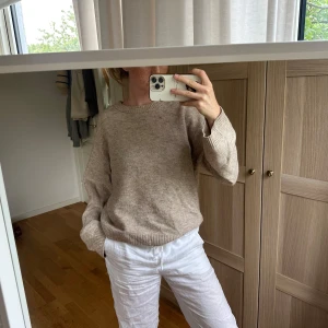 Beige stickad tröja med loose fit från Arket - Supermjuk beige stickad tröja med avslappnad passform och rund hals. Tröjan har ribbade muddar vid ärmslut och nederkant, perfekt för lager-på-lager. Enkel och stilren design som funkar till allt. Snygg att styla med jeans eller kostymbyxor. Liten brun fläck, visas på tredje bilden. 