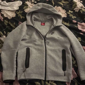 Grå mjukisbyxor från Nike - Snygga grå mjukisbyxor från Nike med svarta detaljer och dragsko i midjan. Byxorna har smal passform och dragkedjeförsedda fickor på sidorna. Perfekta för chill eller träning, med klassisk Nike-logga på benet.