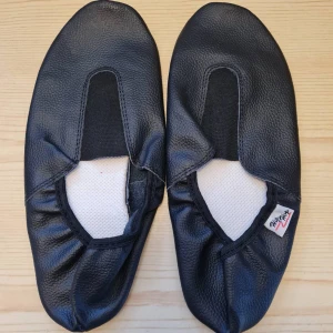 Svarta gymnastikskor i skinn strl 38 (Helt nya) - Säljer ett par helt nya svarta gymnastikskor i äkta läder som aldrig används. De har en enkel design med runt tå och elastisk öppning för enkel på- och avtagning. Perfekta för inomhusaktiviteter och träning.   Storlek 38.  Kan hämtas i Vallentuna.