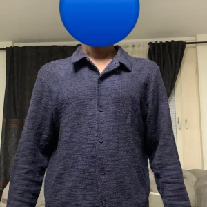 Mörkblå overshirt med knappar - Säljer en stilren mörkblå overshirt med klassisk krage och knäppning framtill. Skjortan har lång ärm och är tillverkad i ett mjukt, strukturerat material som ger en avslappnad men snygg look. Perfekt att bära över en t-shirt eller tröja.