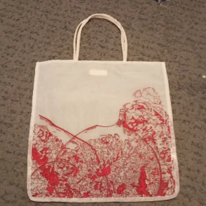 Vit shoppingväska med röd print från Zara - Vit shoppingväska från Zara i tunn bomull med röda konstnärliga tryckdetaljer på båda sidor. Väskan har dubbla handtag och är lätt och smidig att bära med sig till skolan eller stan. Perfekt för dig som gillar unik design och vill ha en väska som sticker ut.