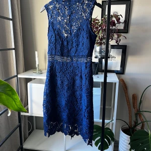 Marinblå spetsklänning PrettyLittleThing - Säljer en marinblå klänning från PrettyLittleThing med vacker blommig spets och transparenta detaljer i midjan. Ärmlös modell med rund hals och figurnära passform. 