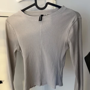 Beige ribbad långärmad tröja från H&M - Säljer en stilren beige långärmad tröja från NLY med ribbad struktur. Tröjan har en rak passform och rund halsringning, perfekt att matcha med jeans eller kjol. Enkel och clean look som funkar året runt.