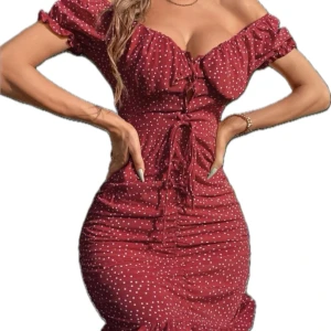 Röd prickig kortklänning med snörning - Supersöt röd kortklänning med vita prickar och offshoulder-ärm. Klänningen har snörning framtill, rynkade detaljer längs hela kroppen och volangkant nertill. Figurnära passform och puffiga korta ärmar ger en romantisk vibe. Perfekt för dig som vill sticka ut!
