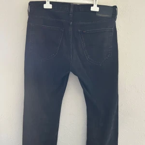 Svarta jeans från Lee straight fit - Säljer ett par svarta jeans från Lee med klassisk femficksdesign och raka ben. Jeansen har en mörk tvätt och subtila slitningar för en cool look. Perfekta för dig som gillar en enkel och tidlös stil. Nypris 800. W31 L32