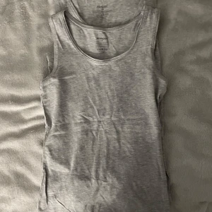 Grå linnetopp från Newbody XS - Säljer en enkel och stilren grå linnetopp från Newbody i storlek XS. Toppen är ärmlös med rund halsringning och tillverkad i mjuk bomullsblandning som känns skön mot huden. Perfekt att matcha med jeans eller shorts för en avslappnad look.