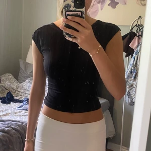 Svart croppad topp med öppen rygg - Säljer en svart croppad topp med tight passform och öppen rygg. Toppen har korta ärmar och en smal rem över ryggen som ger en snygg och modern look. 