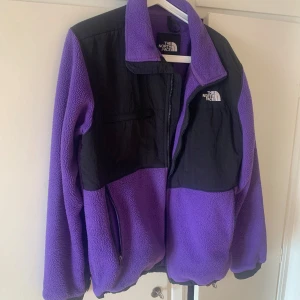Lila fleecejacka från The North Face - Säljer en riktigt snygg lila och svart fleecejacka från The North Face. Jackan har dragkedja framtill, höga fickor och logga på bröstet och ryggen. Perfekt för kyliga dagar och har en sportig vibe med sin kontrastdesign och mjuka fleece.