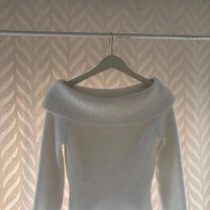 Vit fluffig offshoulder stickad tröja - Supermjuk och fluffig vit stickad tröja med bred offshoulder-krage. Långärmad och perfekt för dig som vill ha en mysig men ändå stilren look. Passar till jeans eller kjol för en trendig vibe.