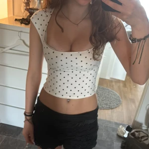 Vit prickig topp - Superfin vit topp med  svarta prickar. Toppen har breda axelband, fyrkantig urringning. Tyvärr har den en liten fläck(kolla sista bilden!) Köpt på Vinted men säljer den vidare då den var för kort!