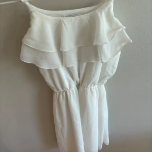 Vit volangklänning med smala axelband - Supersöt vit kortklänning med dubbla volanger upptill och smala axelband. Klänningen har resår i midjan för en snygg passform och är perfekt för sommarens alla tillfällen. Lätt och luftig känsla.