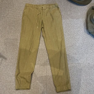 Olivgröna byxor från MNG  - olivgröna byxor från MNG med elastisk midja och snörning framtill. Byxorna har raka ben med resår vid benslut och bälteshällor. 