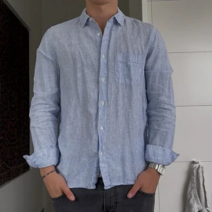 Blåvit randig linneskjorta från Zara - Snygg blåvit randig skjorta från Zara i luftig linnemix. Klassisk krage, bröstficka och knäppning framtill. Perfekt till jeans eller shorts för en chill och stilren look. Långärmad modell med relaxed fit.