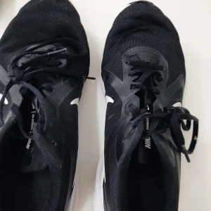 Svarta Nike löparskor med vit sula - Priset kan förhandlas. Svarta Nike sneakers med vit sula och klassisk vit swoosh på sidan. Ovandelen är i mesh för bra andningsförmåga och skorna har snörning. Perfekta för löpning eller träning, med sportig look och bekväm passform.