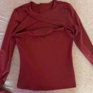 Vinröd omlottopp med lång ärm - Snygg vinröd topp med omlottdetalj över bröstet och lång ärm. Toppens material är stretchigt och figurnära, perfekt för att skapa en cool och trendig look. Passar dig som gillar unika detaljer och vill sticka ut lite extra. Den röda färgen är mörkare i verkligheten. Helt ny.