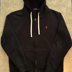 Svart hoodie från Polo Ralph Lauren XL - Säljer en svart hoodie från Polo Ralph Lauren med dragkedja. Den är bara testad, så den är i riktigt fint skick. Står XL i den, men skulle säga att den passar bättre som en L – lite mindre i modellen.