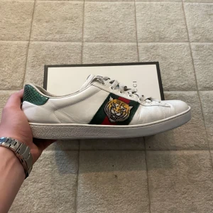 Gucci ace  - Gucci sneakers i vitt skinn med klassiska gröna och röda ränder på sidan och en broderad tiger. Grön detalj i mocka på hälen. Snygg och unik design som sticker ut, levereras med originalkartong och dustbag. Kvitto medföljer också 