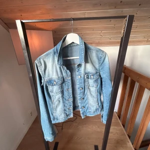 Ljusblå jeansjacka med knappar - Snygg ljusblå jeansjacka från only med klassisk krage och knäppning framtill. Jackan har två bröstfickor med lock och knappar samt långa ärmar. Perfekt för dig som vill ha en tidlös och cool look.