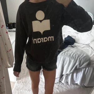 Svart Marant sweatshirt med tryck - Cool svart sweatshirt från Marant med stort vitt logotryck framtill. Som ni ser så har trycket lossnat lite på andra bilden, därav de låga priset. Storlek 40 men passar mig som bär Xs/s då jag upplever att den är mycket liten i storleken 