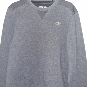 Blågrå tröja från Lacoste - Blågrå sweatshirt från Lacoste med deras ikoniska krokodillogga på bröstet. Tröjan har långa ärmar och en rund halsringning.