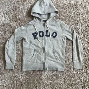 Ralph Lauren hoodie - Tjena! En grå hoodie från Ralph Lauren med dragkedja och stor text på bröstet. Polo texten ska vara så! Skick 10/10, pris kan diskuteras🌟