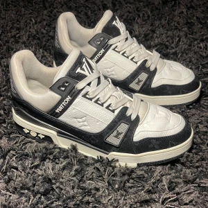 Svartvita sneakers från Louis Vuitton - Snygga svartvita sneakers från Louis Vuitton med märkets ikoniska logga på tungan och hälen. Skorna har en stilren design med snörning och en bekväm passform. Perfekta för dig som vill ha en lyxig touch i vardagen. De är uk 7 i storlek