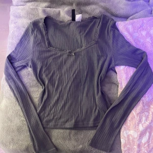 Grå topp - Säljer en stilren grå ribbad topp med spetsdetaljer vid halsringningen. Toppen har långa ärmar och en elegant passform. Perfekt för en chic vardagslook.