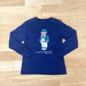 Ralph lauren polo tröja - Säljer en snygg blå långärmad tröja från Ralph Lauren med en cool Polo Bear-design på framsidan. Perfekt för en avslappnad stil med en touch av elegans. Tröjan är i storlek M och passar perfekt för höst och vår. 10-12 år. Jättebra skick.