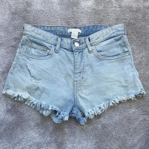 Ljusblå jeansshorts från H&M - Snygga ljusblå jeansshorts från H&M med fransiga kanter och klassisk femficksdesign. Perfekta för sommardagar och avslappnade stunder. De har en knapp och dragkedja framtill för enkel stängning.