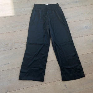 Svarta vida byxor från 1.57 - Snygga svarta byxor från 1.57 med en loose passform och elastisk midja. Byxorna har en bred och bekväm design som ger en avslappnad stil. Perfekta för en stilren look.