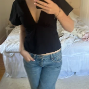 Svart v-ringad topp - Snygg svart v-ringad topp med korta ärmar. Perfekt för en stilren look. Passar bra till både jeans och kjol. Ja har en nål vid tröjan som ja satt på just vid de tillfället så ni ej tror de en del av tröjan, rosett där bak!