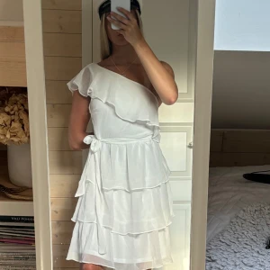 Vit oneshoulder klänning - Säljer en söt vit oneshoulder klänning med volanger. Klänningen har ett knytband i midjan o är perfekt till student, skolavslutningen eller annat💕helt oanvänd 