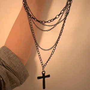 Svart halsband med kors - Snyggt svart halsband med flera kedjor och ett hängande kors. Perfekt för att ge en edgy touch till din outfit. Kedjorna har olika längder för en lager-på-lager-effekt.