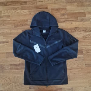 Svart Nike Tech Fleece  - Nike Tech Fleece Hoodie – Old Design (S)  Säljer en svart Nike Tech Fleece hoodie i storlek S. Äldre design som inte längre säljs, vilket gör den unik och svår att hitta.  ✅ Mycket bra skick – sparsamt använd ✅ Lätt, varm & bekväm med Tech Fleece-teknologi ✅ Storlek S (slim fit, passar S eller tight M) ✅ Klassisk zip-hoodie med fickor  📦 Snabb leverans – skickas samma dag! 📦 📌 Kontakta mig vid intresse eller funderingar📌  
