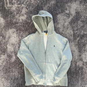Grå hoodie från Polo Ralph Lauren - Säljer en stilren grå hoodie från Polo Ralph Lauren med dragkedja och det klassiska logotypbroderiet på. Tröjan passar perfekt till storleken Xs men kan även funka vid S beroende på längd. Inga defekter! 